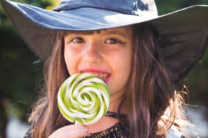 girl in a witch costume eating a lollipop on Halloween